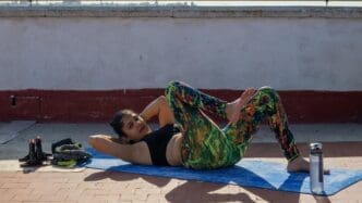 A woman exercises on a rooftop with a cityscape in the background.