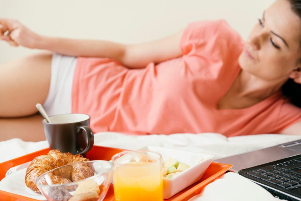 A woman reclines on a bed next to a breakfast tray.