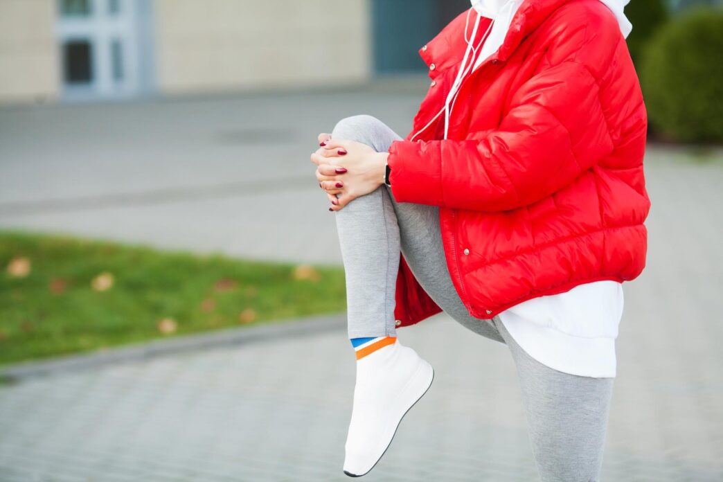 A woman stretches her body, performing exercises on a street.