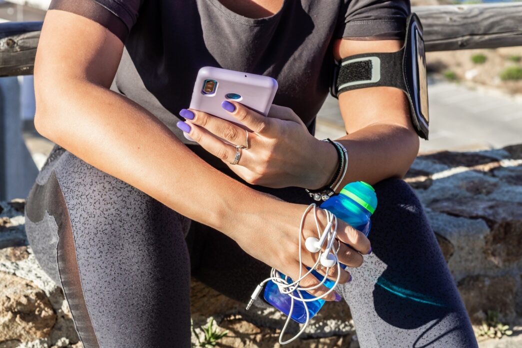 A young woman athlete sits on the floor, focused on her mobile phone.
