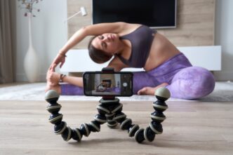 Young woman in athletic wear records a yoga video in her living room.