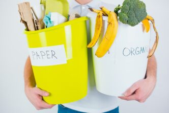 Close-up of a young man's hands holding buckets of organic and paper waste for recycling against a white background.
