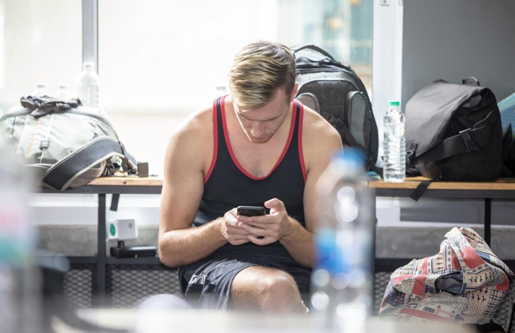 A young man sits in a gym, looking at his mobile phone.