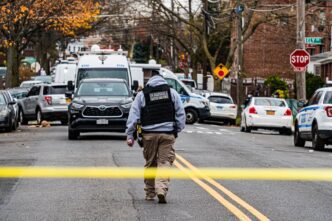 A federal agent in a crime scene with police vehicles and tape in an urban neighborhood.