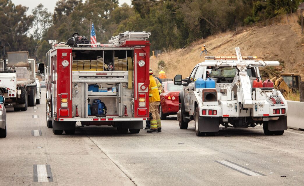 A fire truck and tow truck are stopped on a freeway at an accident scene with a fireman visible, photographed by F Armstrong.