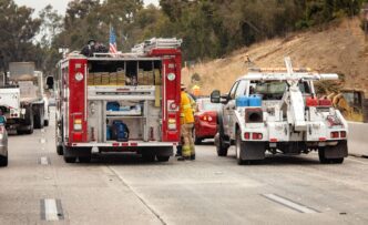 A fire truck and tow truck are stopped on a freeway at an accident scene with a fireman visible, photographed by F Armstrong.