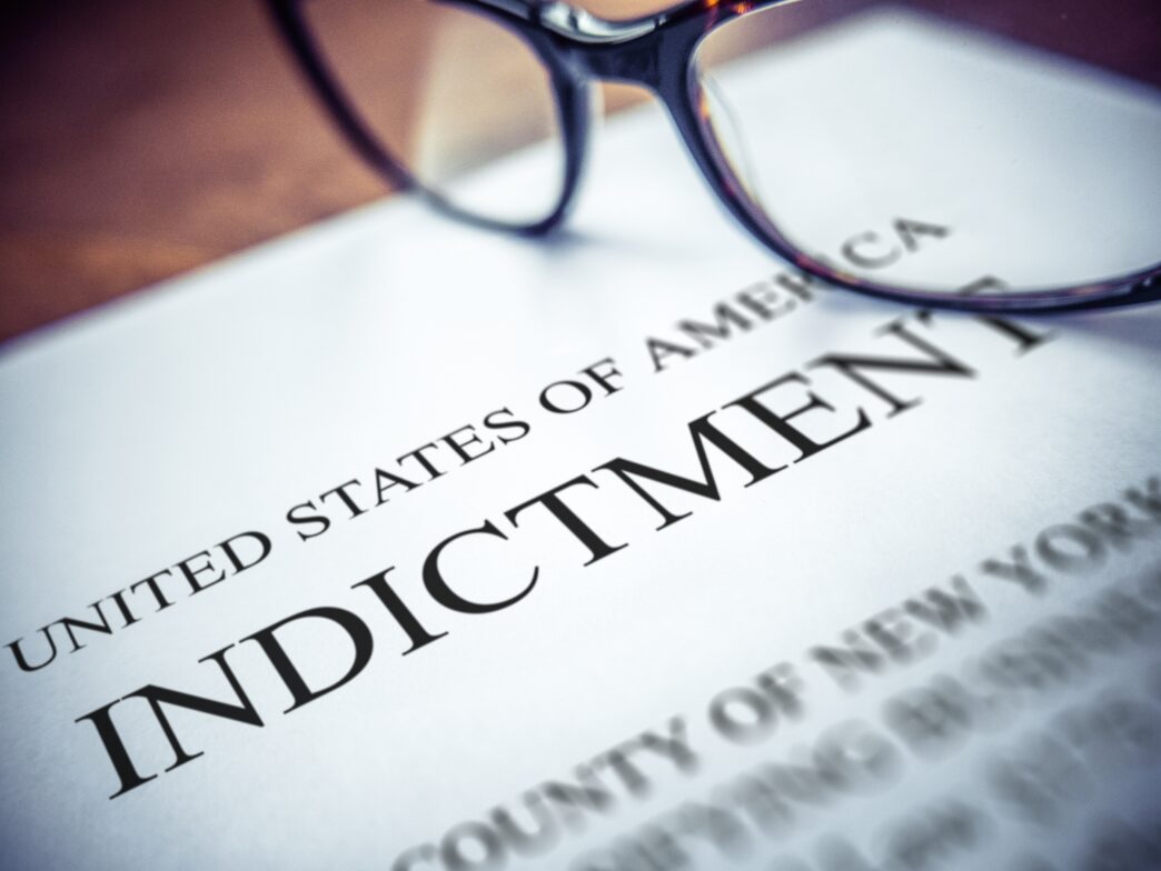 An indictment document titled "Indictment" lies on a desk with glasses, captured with shallow focus by Mr. Doomits.