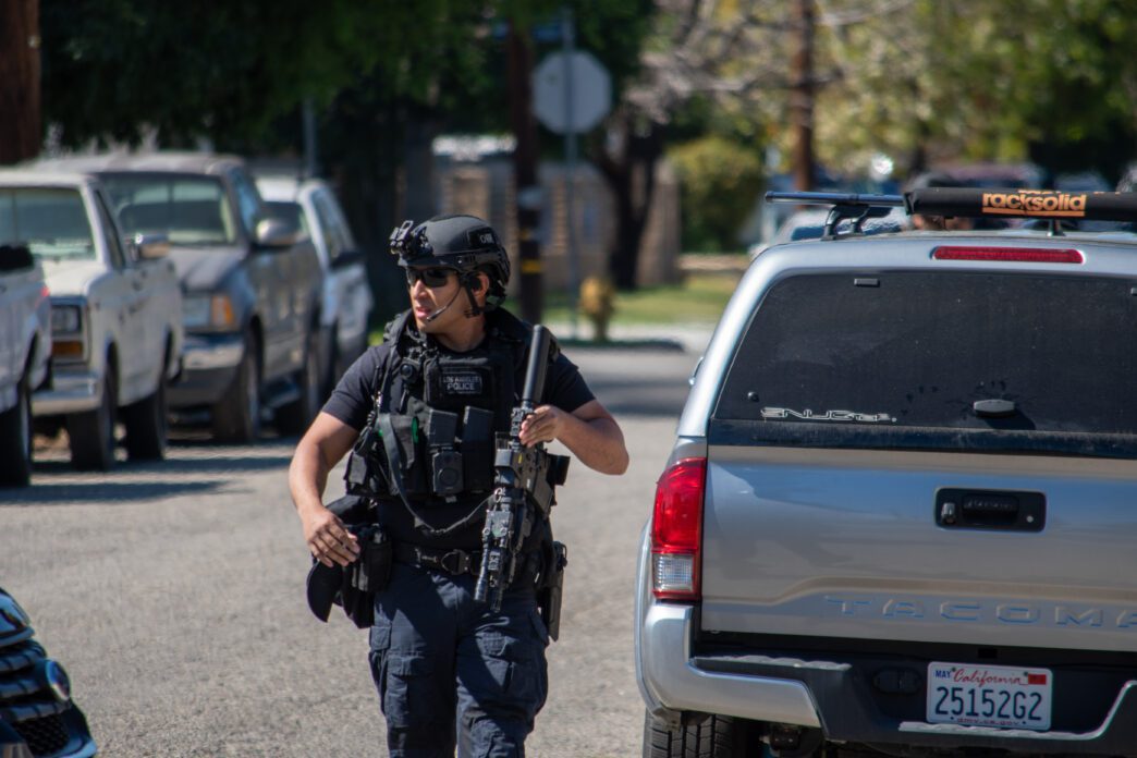 An armed SWAT officer moves tactically down a suburban street.