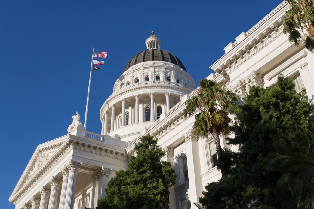 California State Capitol Building in Sacramento with palm trees and flags.