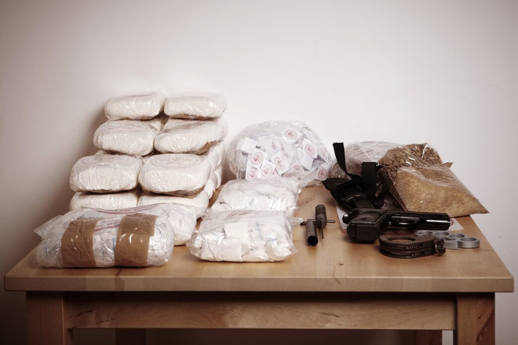 Drugs and weapons seized by police displayed on a table, captured by Couperfield-Shutterstock.