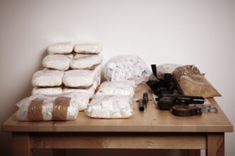 Drugs and weapons seized by police displayed on a table, captured by Couperfield-Shutterstock.