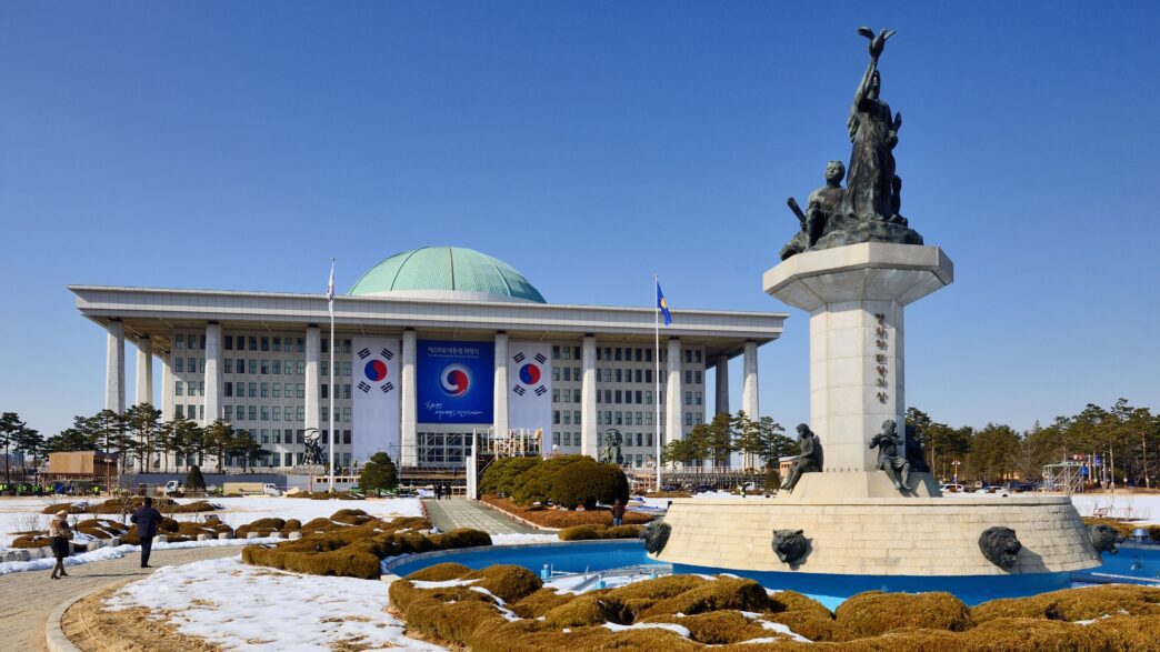 National Assembly of the Republic of Korea with a prominent statue and snowy landscape in front.
