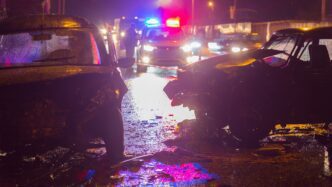 Nighttime car crash scene illuminated by police lights with damaged vehicles on a road.