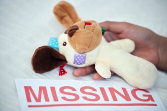 A hand holds a stuffed toy near a paper with "MISSING" printed, highlighting concern for missing children.