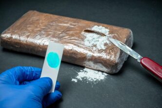 Police officer holds positive cocaine drug test strip near a package.
