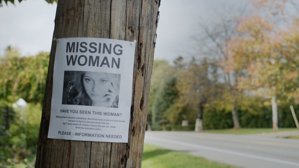 A missing young woman's poster is attached to a pole near the road.
