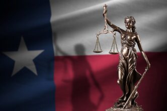 Lady Justice statue and scales in front of the Texas state flag in a dark room.