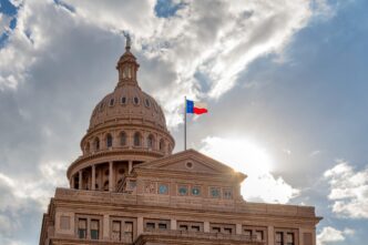 The Texas State Capitol Building in Austin at sunset with the Texas flag waving.