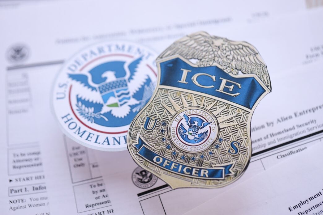 A US ICE officer badge and Department of Homeland Security seal on USCIS immigration forms close-up.