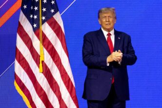 US President Donald J. Trump stands beside an American flag.