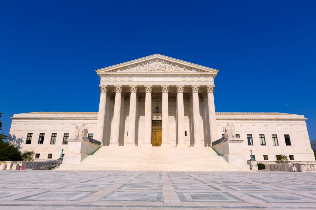 The United States Supreme Court Building with its grand columns under a clear blue sky.