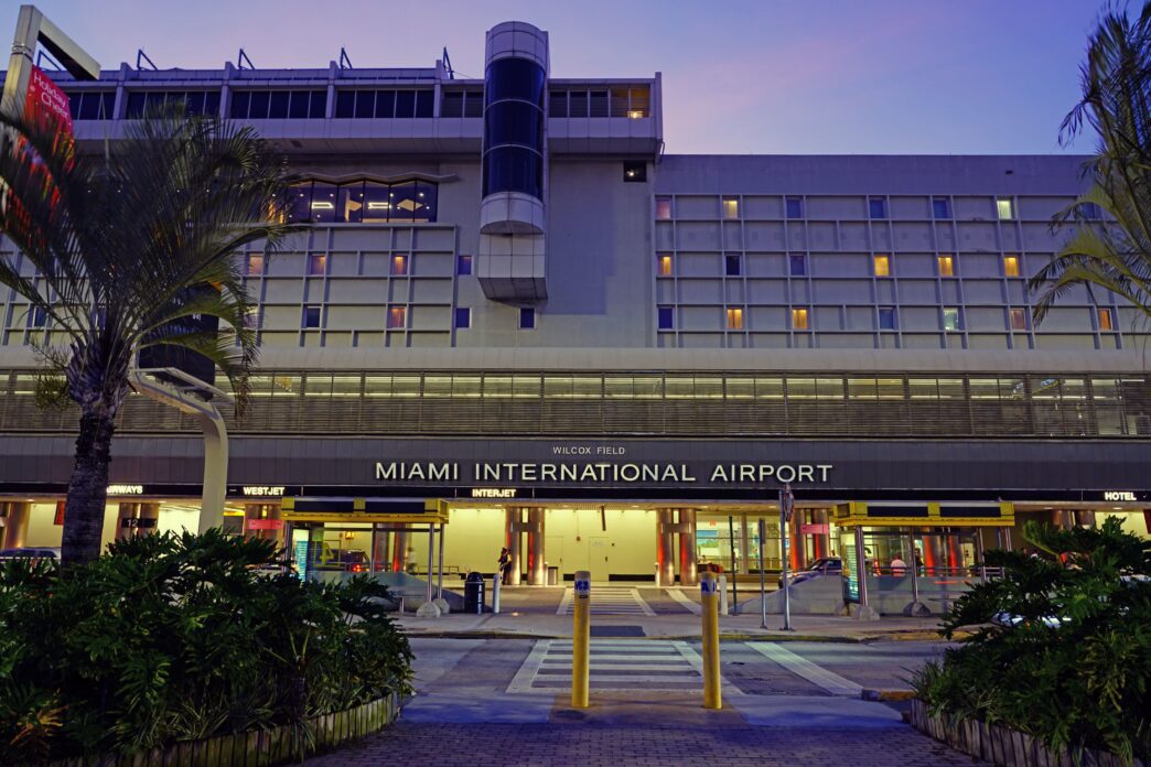 Main entrance of Miami International Airport at dusk with palm trees and lit windows.