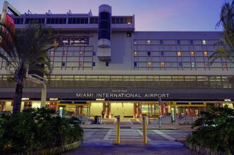 Main entrance of Miami International Airport at dusk with palm trees and lit windows.