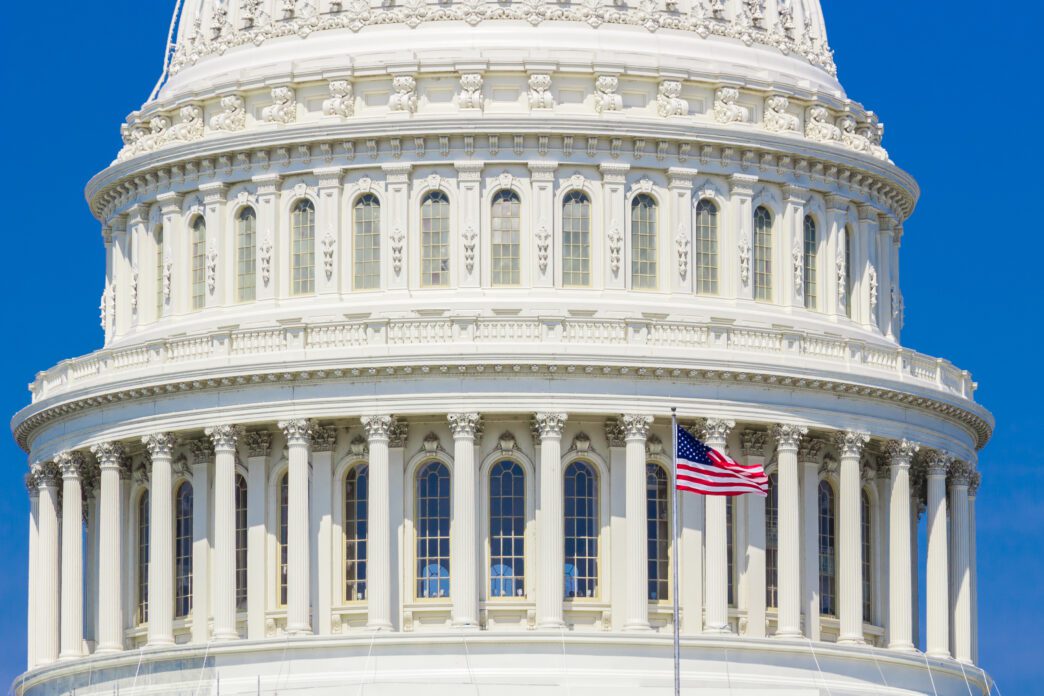 American flag flying against the Capitol Building under blue sky