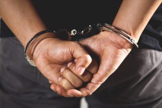 Male criminal in handcuffs standing with hands behind back.