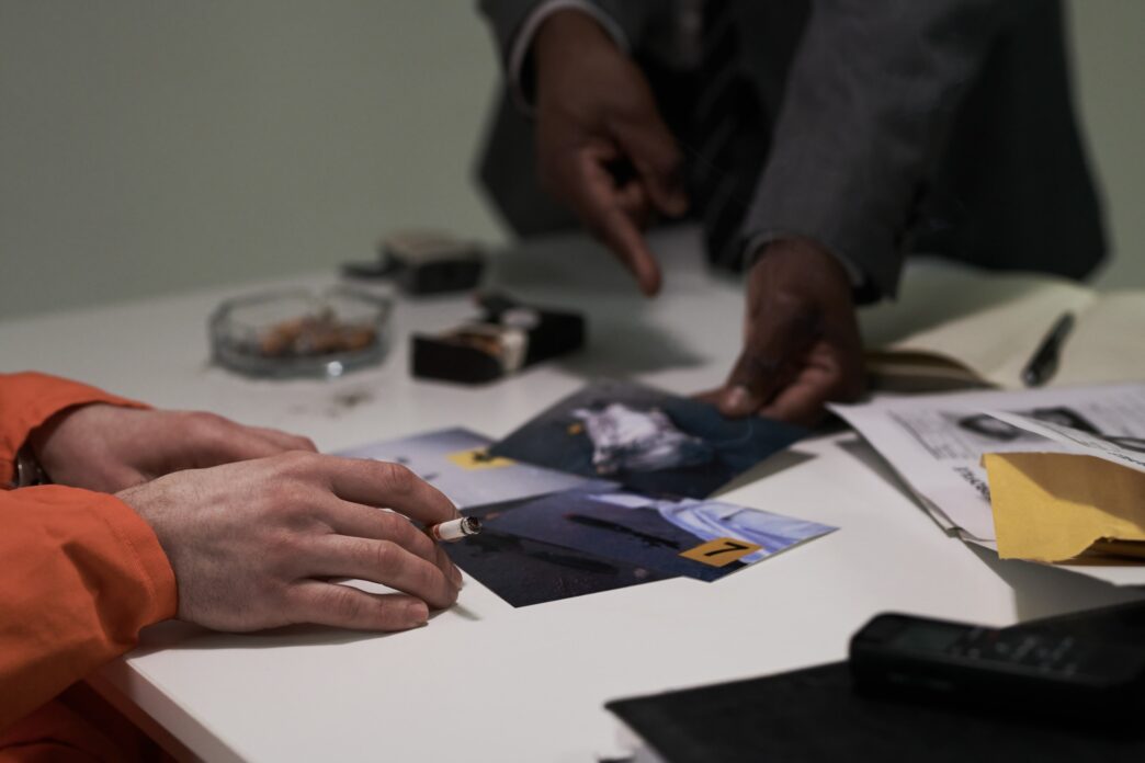 Two individuals examine crime scene evidence photographs on a table.