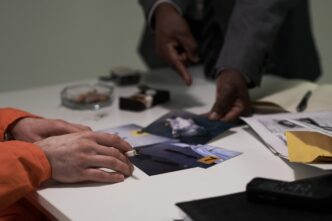 Two individuals examine crime scene evidence photographs on a table.