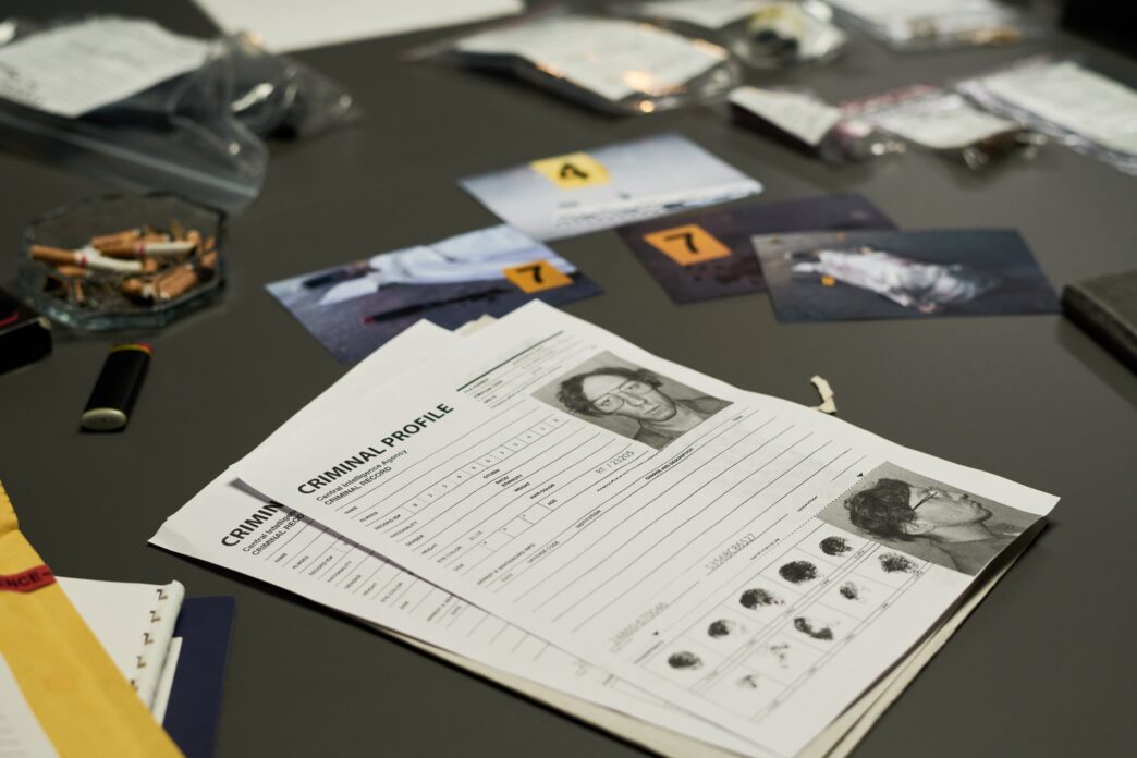 Evidence files and criminal profiles are organized on a desk for an investigation.