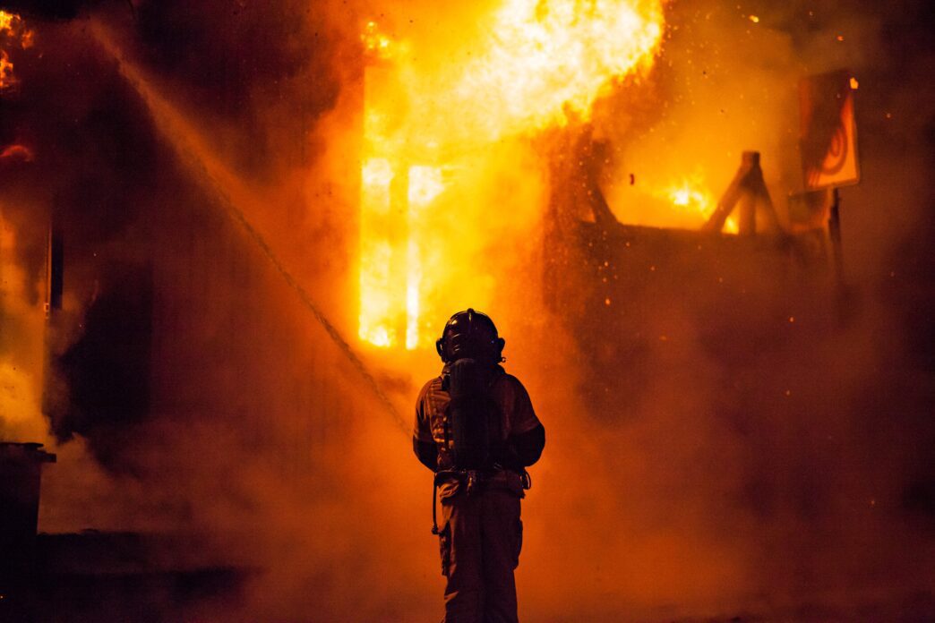 Rear view of a firefighter battling a blaze at night with intense flames.