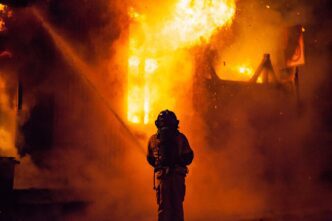 Rear view of a firefighter battling a blaze at night with intense flames.