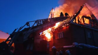 Firefighters extinguish a house fire in a village, using a crane amidst smoke and sparks.