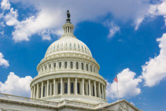 The US Capitol dome with an American flag under a blue sky.