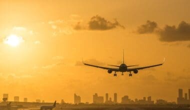 At sunrise, an airplane descends for a landing at Miami International Airport, with the Miami Downtown skyline forming a stunning backdrop