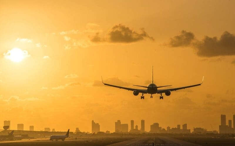 At sunrise, an airplane descends for a landing at Miami International Airport, with the Miami Downtown skyline forming a stunning backdrop